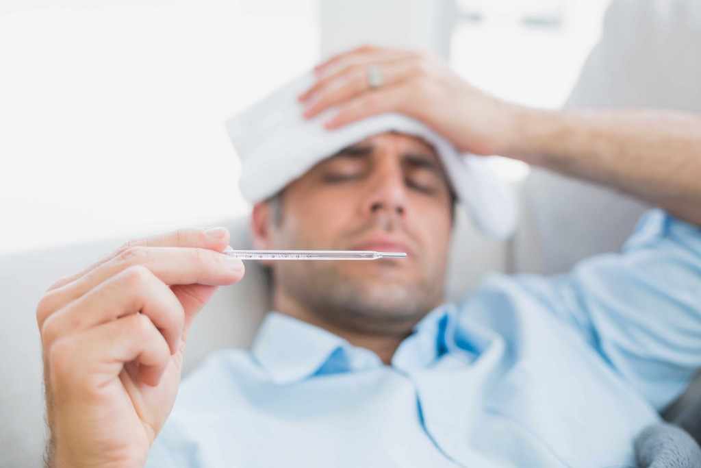 a man with a fever checking his temperature with a thermometer